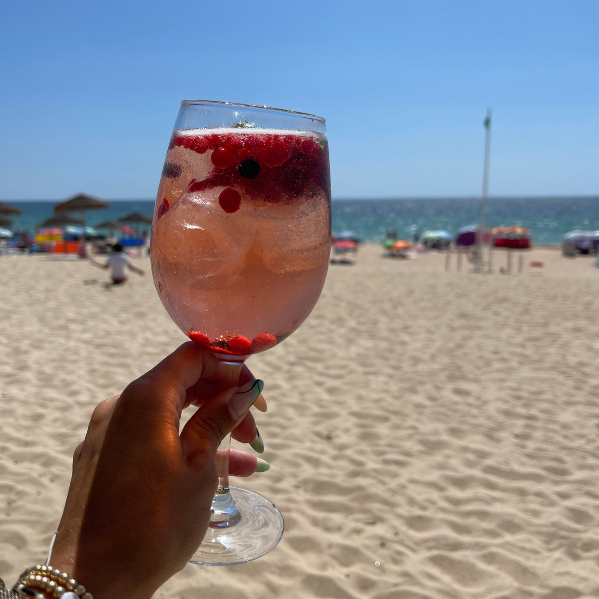 Hand holding a wine glass with red berries on a beach